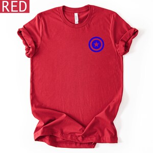 Pu&ograve; includere: T-shirt rossa con grafica blu e bianca sul petto in alto a sinistra. La grafica &egrave; un cerchio blu con una stella blu al centro. La parola "RED" &egrave; in una casella bianca nell'angolo in alto a sinistra.
