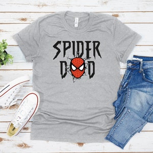K&ouml;nnte beinhalten: Graues T-Shirt mit einer roten und schwarzen Spider-Man-Grafik und dem Text "Spider Dad" in Schwarz.