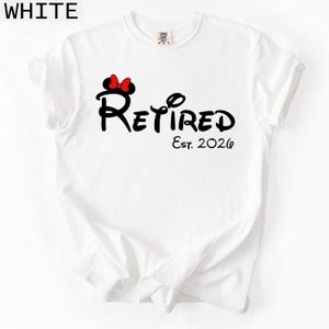 Puede incluir: Camiseta blanca con la palabra "Retired" en escritura negra, con un lazo rojo y el texto "Est. 2026". La palabra "WHITE" est&aacute; impresa en la esquina superior izquierda de la imagen.
