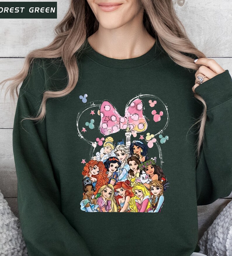 以下が含まれることがあります： ディズニーのプリンセスとピンクのドット柄のリボンが描かれた、フォレストグリーンのスウェットシャツ。デザインには、ミッキーマウスの耳の白いアウトラインとカラフルな蝶が含まれています。スウェットシャツは快適でカジュアルなスタイルです。