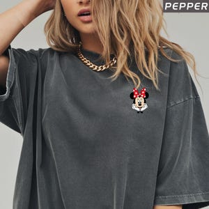 May include: Dark grey t-shirt with a small Minnie Mouse graphic on the chest. The graphic shows Minnie Mouse with a red bow with white polka dots. The word "PEPPER" is printed in white in the upper right corner.