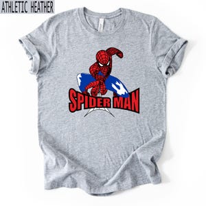 Op de afbeelding: Athletic heather grijs t-shirt met een Spider-Man afbeelding. Het ontwerp bevat een rood en zwart Spider-Man figuur, een blauw webdesign en de rode tekst "SPIDER-MAN".