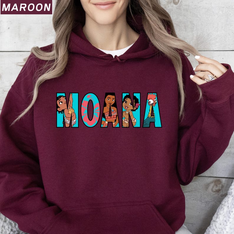 May include: A maroon-coloured hoodie with the word "MOANA" in turquoise block letters. The letters contain cartoon illustrations. The hoodie has a drawstring hood and a kangaroo pocket.