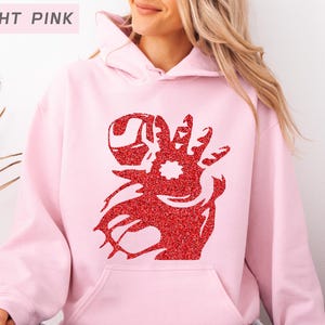 May include: Light pink hoodie with a red glitter design on the front. The design appears to be a stylized hand with a star in the center. The text "LIGHT PINK" is in a rectangular box in the upper left corner.