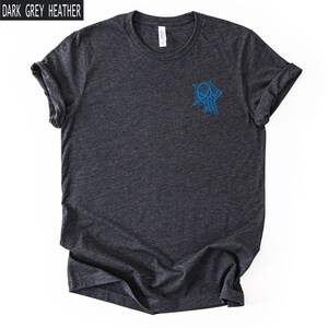 Op de afbeelding: Een donkergrijs gem&ecirc;leerd T-shirt met korte mouwen en een ronde hals. Het shirt heeft een kleine blauwe afbeelding op de linkerborst met een gestileerd spinnenmasker en webontwerp. De tekst "DARK GREY HEATHER" staat in de linkerbovenhoek.