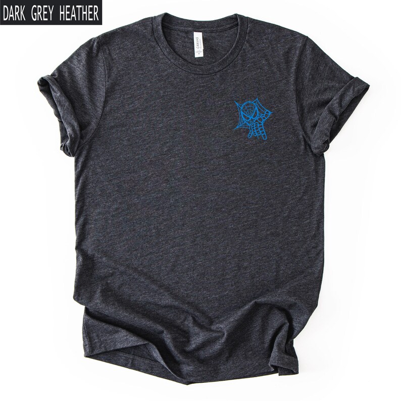Op de afbeelding: Een donkergrijs gem&ecirc;leerd T-shirt met korte mouwen en een ronde hals. Het shirt heeft een kleine blauwe afbeelding op de linkerborst met een gestileerd spinnenmasker en webontwerp. De tekst "DARK GREY HEATHER" staat in de linkerbovenhoek.