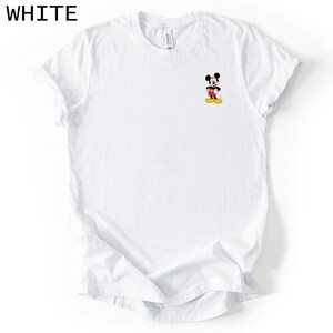 May include: A white short-sleeved t-shirt featuring a small graphic of Mickey Mouse on the left chest area. The character is depicted in his classic black, red, and yellow colours. The shirt has a crew neckline and a standard fit design.