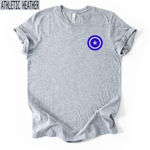 Pu&ograve; includere: T-shirt grigio atletico con un'emblema a stella blu e bianca sul petto sinistro. La maglietta ha un girocollo e maniche corte. Il testo "ATHLETIC HEATHER" &egrave; in alto.