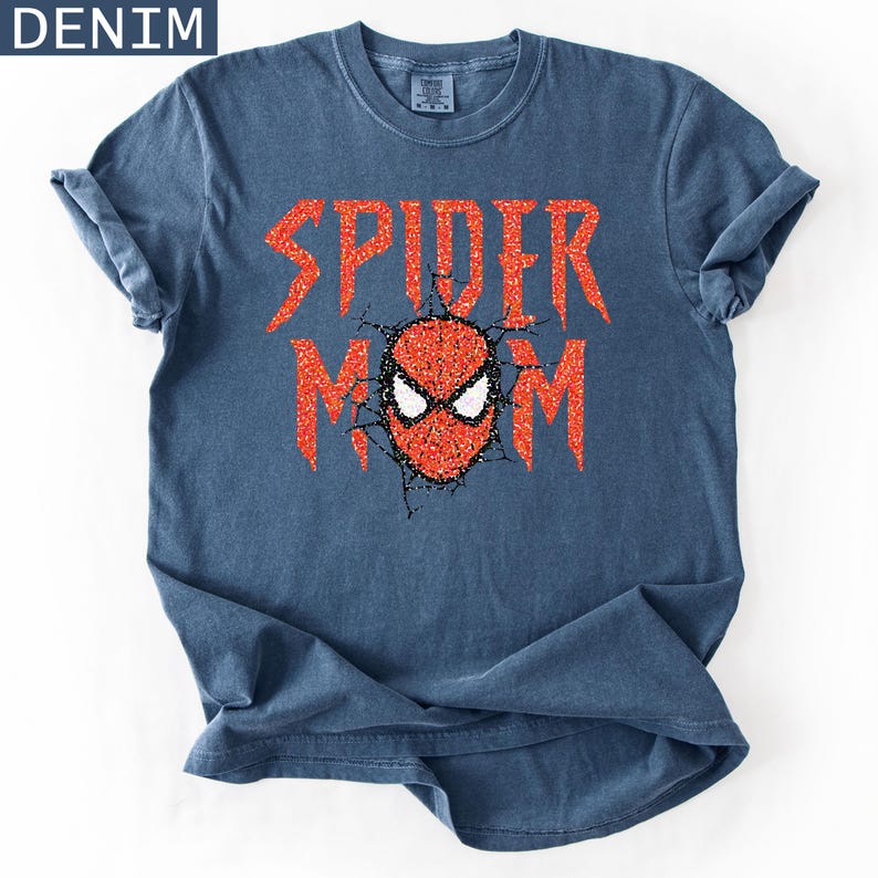 May include: A denim blue t-shirt with rolled sleeves. The shirt features the text "SPIDER MOM" in red glitter lettering, with a red and white spider-man mask graphic in the center. The word "DENIM" is in the upper left corner.