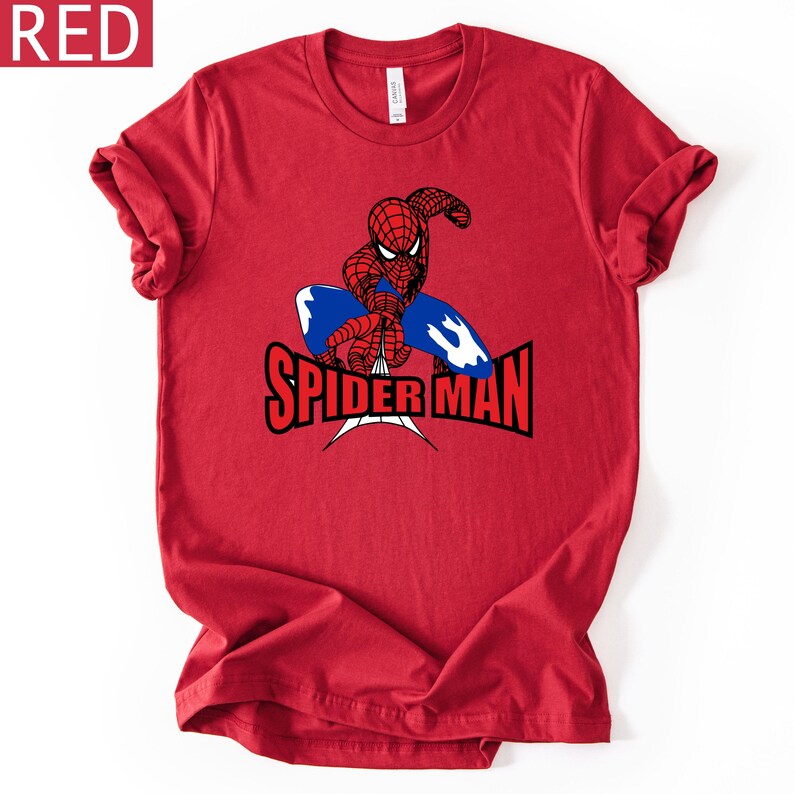 Op de afbeelding: Rood t-shirt met een Spider-Man afbeelding. Het ontwerp toont Spider-Man in een dynamische pose met een blauw en wit webachtig element. De woorden "SPIDER MAN" zijn vetgedrukt, zwart en rood.