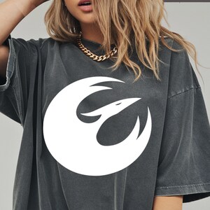 May include: Dark gray oversized t-shirt featuring a white graphic of a bird within a circle. The shirt has short sleeves and a slightly faded appearance. The word "PEPPER" is printed in white in the upper right corner.