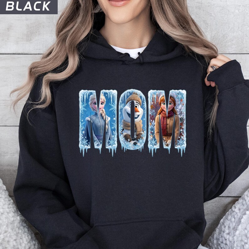 Puede incluir: Sudadera con capucha negra con la palabra "MOM" en letras azul hielo. Las letras presentan im&aacute;genes de personajes de la pel&iacute;cula Frozen. La sudadera es de color oscuro.