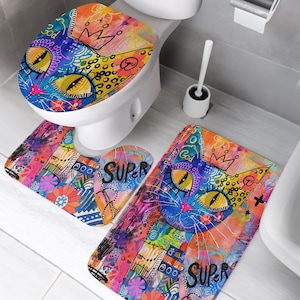 May include: A colorful bathroom set featuring a cat design. The set includes a toilet seat cover, a U-shaped rug, and a rectangular rug. The cat design is in shades of blue, yellow, orange, and pink, with the word "SUPER" on the rugs.