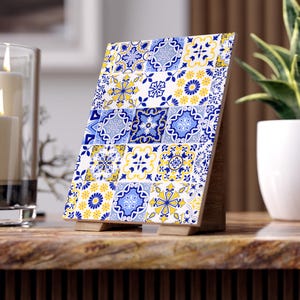 Könnte beinhalten: Eine dekorative Holzfliese mit einem sich wiederholenden Muster aus blauen und gelben Blumen- und geometrischen Designs. Die Fliese wird von einem Holzständer getragen, der ihre komplizierten Details und ihre farbenfrohe Ästhetik hervorhebt. Ein einzigartiger Einrichtungsgegenstand.
