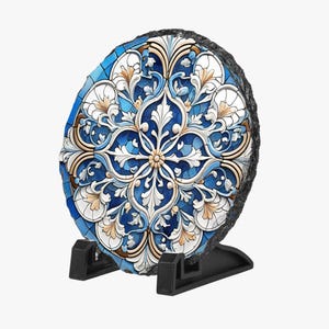 Könnte beinhalten: Ein runder, dekorativer Stein mit einem detaillierten floralen Design in Blau-, Weiß- und Goldtönen. Der Stein ist auf einem schwarzen Ständer montiert, der die komplizierten Muster und Texturen hervorhebt. Das Design zeigt symmetrische, stilisierte Blätter und Blütenblätter.