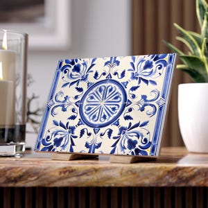 Könnte beinhalten: Dekorative Keramikfliese mit blau-weißem Blumenmuster. Die Fliese hat ein zentrales kreisförmiges Motiv und wird von zwei kleinen Holzständern getragen. Die Fliese wird auf einer Marmoroberfläche präsentiert.