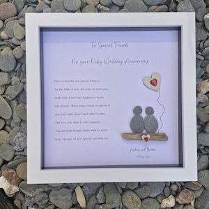 May include: A framed white and grey picture with a message for a couple celebrating their 40th wedding anniversary. The message reads "To Special Friends On your Ruby Wedding Anniversary." The picture includes a couple made of grey stones, a red heart balloon, and a piece of driftwood.