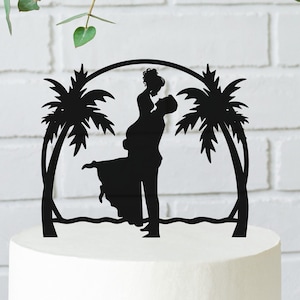 May include: Black silhouette cake topper of a couple kissing under palm trees on a beach. The couple is silhouetted against a white background.