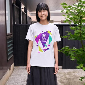 Puede incluir: Una camiseta blanca de manga corta con un dise&ntilde;o gr&aacute;fico central que muestra el logotipo de Taco Bell en blanco, rodeado de formas triangulares geom&eacute;tricas en morado, verde azulado y verde lima. La camiseta se combina con una falda negra.
