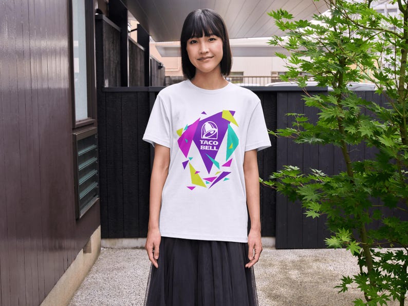 Puede incluir: Una camiseta blanca de manga corta con un dise&ntilde;o gr&aacute;fico central que muestra el logotipo de Taco Bell en blanco, rodeado de formas triangulares geom&eacute;tricas en morado, verde azulado y verde lima. La camiseta se combina con una falda negra.