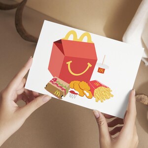 May include: A white card with a red and yellow McDonald's box, a box of Chicken McNuggets, a box of fries, and a cup of soda. The McDonald's box has a smiling face.