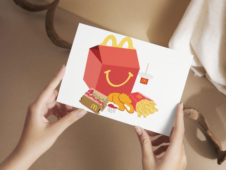 May include: A white card with a red and yellow McDonald's box, a box of Chicken McNuggets, a box of fries, and a cup of soda. The McDonald's box has a smiling face.