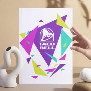 Puede incluir: Una impresi&oacute;n rectangular blanca que presenta el logotipo morado de Taco Bell centrado dentro de un gran tri&aacute;ngulo morado. El dise&ntilde;o est&aacute; rodeado por tri&aacute;ngulos geom&eacute;tricos dispersos en tonos vibrantes de verde lima, magenta y cerceta sobre un fondo blanco.