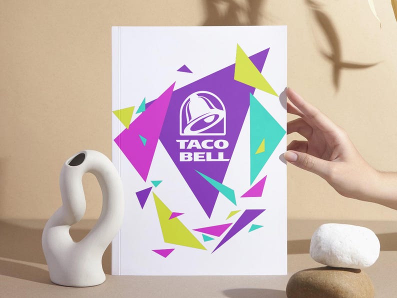 Puede incluir: Una impresi&oacute;n rectangular blanca que presenta el logotipo morado de Taco Bell centrado dentro de un gran tri&aacute;ngulo morado. El dise&ntilde;o est&aacute; rodeado por tri&aacute;ngulos geom&eacute;tricos dispersos en tonos vibrantes de verde lima, magenta y cerceta sobre un fondo blanco.