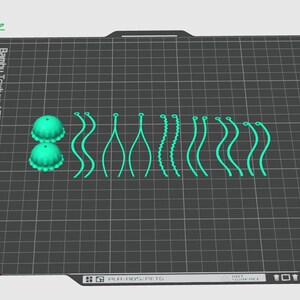 May include: A close-up of a 3D printed design on a textured black surface. The design includes two small green dome-shaped objects and a series of green lines and curves.