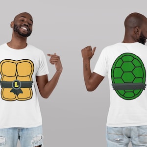 May include: White t-shirt featuring a cartoon design of a turtle shell on the front and back. The front design is yellow with a black belt and the letter "L". The back design is green with a black belt.