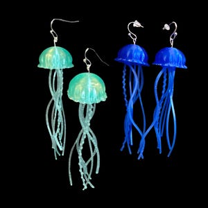 May include: A set of three dangle earrings featuring jellyfish designs. Two earrings are blue and one is green.
