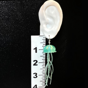May include: Green and blue iridescent jellyfish dangle earrings with silver hooks. The earrings are approximately 2 inches long.