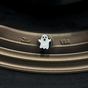 Puede incluir: Un tap&oacute;n de v&aacute;lvula de neum&aacute;tico en forma de fantasma blanco. El tap&oacute;n est&aacute; en una llanta de neum&aacute;tico marr&oacute;n con las palabras "JIL" y "VIA" impresas en la llanta.