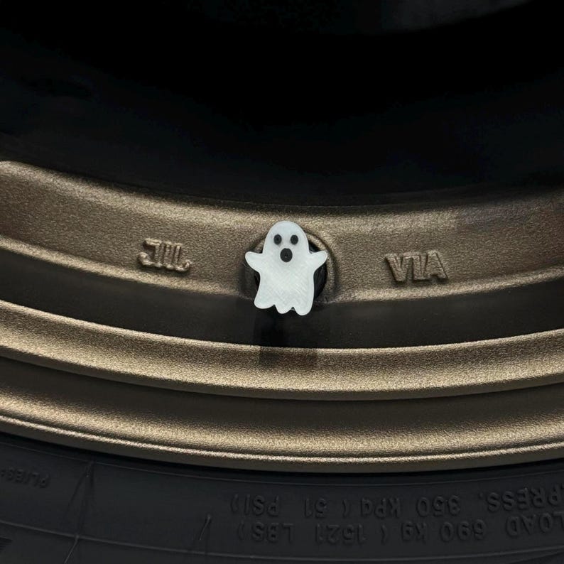 Puede incluir: Un tap&oacute;n de v&aacute;lvula de neum&aacute;tico en forma de fantasma blanco. El tap&oacute;n est&aacute; en una llanta de neum&aacute;tico marr&oacute;n con las palabras "JIL" y "VIA" impresas en la llanta.