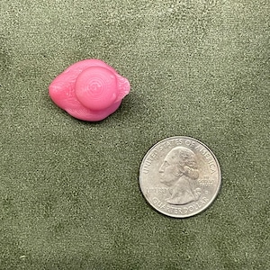Puede incluir: Una figurita de cer&aacute;mica rosa de un p&aacute;jaro con un sombrero. El p&aacute;jaro est&aacute; sentado sobre una superficie de tela verde.