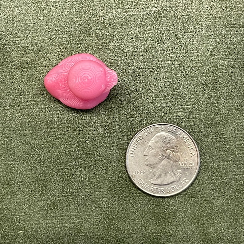 Puede incluir: Una figurita de cer&aacute;mica rosa de un p&aacute;jaro con un sombrero. El p&aacute;jaro est&aacute; sentado sobre una superficie de tela verde.