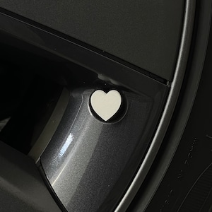 Puede incluir: Un tapón de válvula de neumático de coche en forma de corazón blanco.