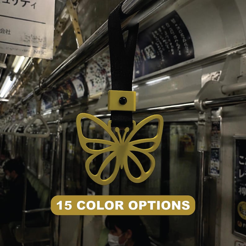May include: A yellow butterfly-shaped handle for a subway or train, hanging from a black strap. The handle is attached to a metal bar. The image includes the text "15 COLOR OPTIONS" in a yellow banner.
