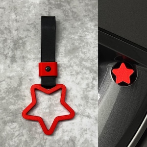 May include: Red star-shaped car handle with a black strap. The handle is attached to a red star-shaped screw cap.