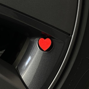 May include: A red heart-shaped valve stem cap for a car tire.