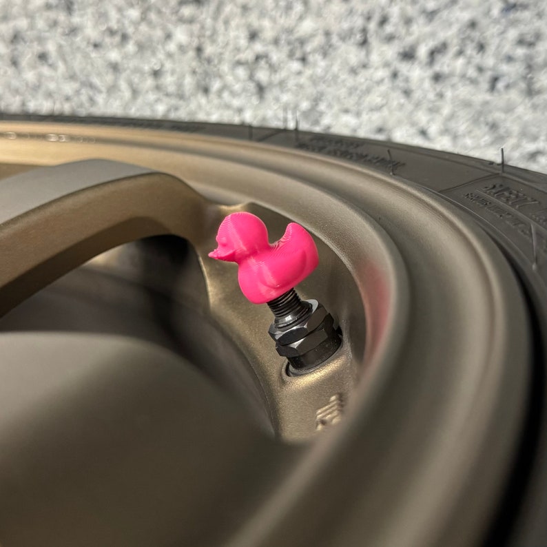 Puede incluir: Un tap&oacute;n de v&aacute;lvula de tallo de goma de pato rosa en una rueda de coche marr&oacute;n.