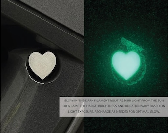 Puede incluir: Un tapón de válvula en forma de corazón plateado brilla en verde en la oscuridad después de haber sido expuesto a la luz del sol o a una lámpara.  GLOW-IN-THE-DARK FILAMENT MUST ABSORB LIGHT FROM THE SUN OR A LAMP TO CHARGE. BRIGHTNESS AND DURATION VARY BASED ON LIGHT EXPOSURE. RECHARGE AS NEEDED FOR OPTIMAL GLOW.