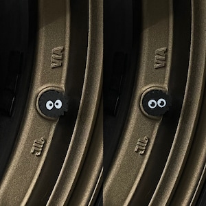 May include: Close-up of two black tyre valve stem caps with white eyes and a black outline. The caps are attached to a brown tyre rim with the word "VIA" printed on the rim.