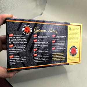 May include: A box of Lilliput World Beer with a Guinness History timeline. The box has a black background with gold and red accents. Text includes historical dates and milestones of Guinness beer.