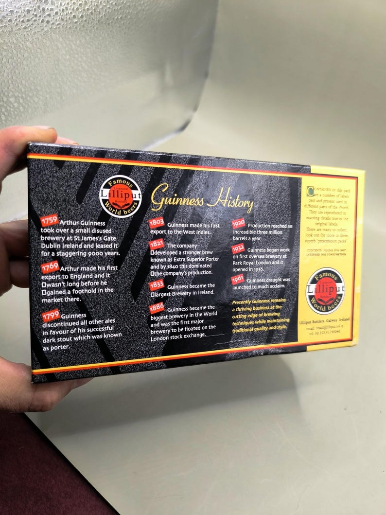 May include: A box of Lilliput World Beer with a Guinness History timeline. The box has a black background with gold and red accents. Text includes historical dates and milestones of Guinness beer.