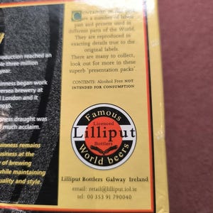 May include: A box with text and a circular logo for Lilliput World Beers. The logo is black, white, and red, with the words "Famous" and "World beers" in a circular design. The text on the box describes the product as a collection of labels from around the world.