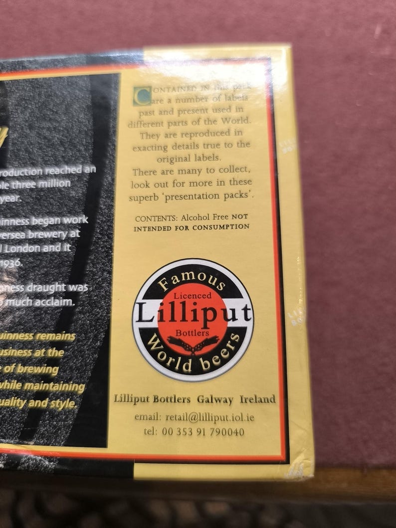 May include: A box with text and a circular logo for Lilliput World Beers. The logo is black, white, and red, with the words "Famous" and "World beers" in a circular design. The text on the box describes the product as a collection of labels from around the world.