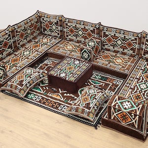 May include: A traditional Middle Eastern floor seating set with brown and green patterned cushions and a matching rug. The set includes a large sofa, several smaller cushions, and a square ottoman.