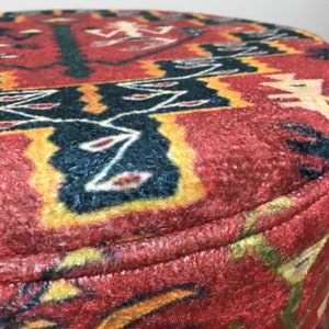 Puede incluir: Primer plano de un puf de tela con estampado rojo, amarillo y negro con base de madera marr&oacute;n.