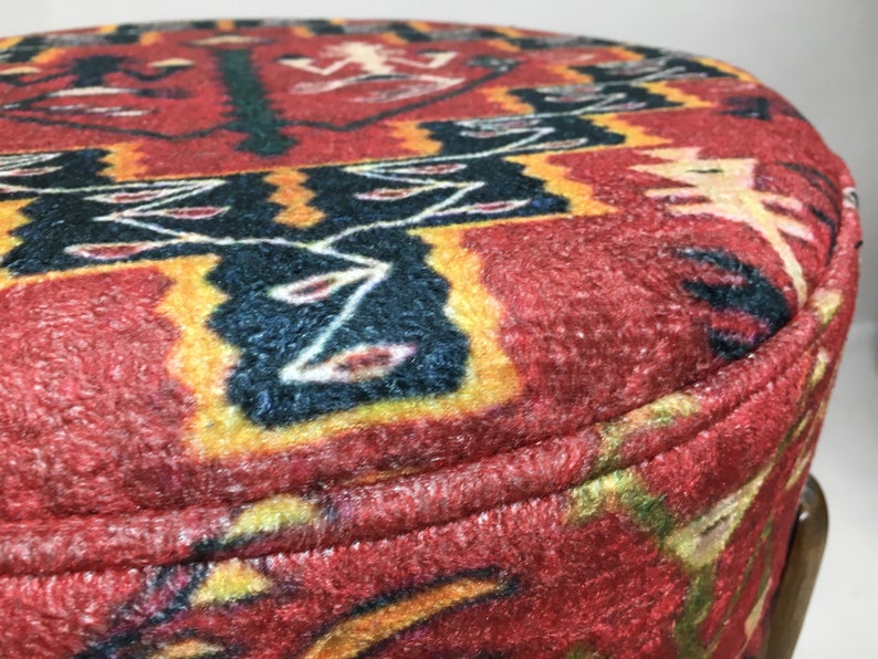 Puede incluir: Primer plano de un puf de tela con estampado rojo, amarillo y negro con base de madera marr&oacute;n.